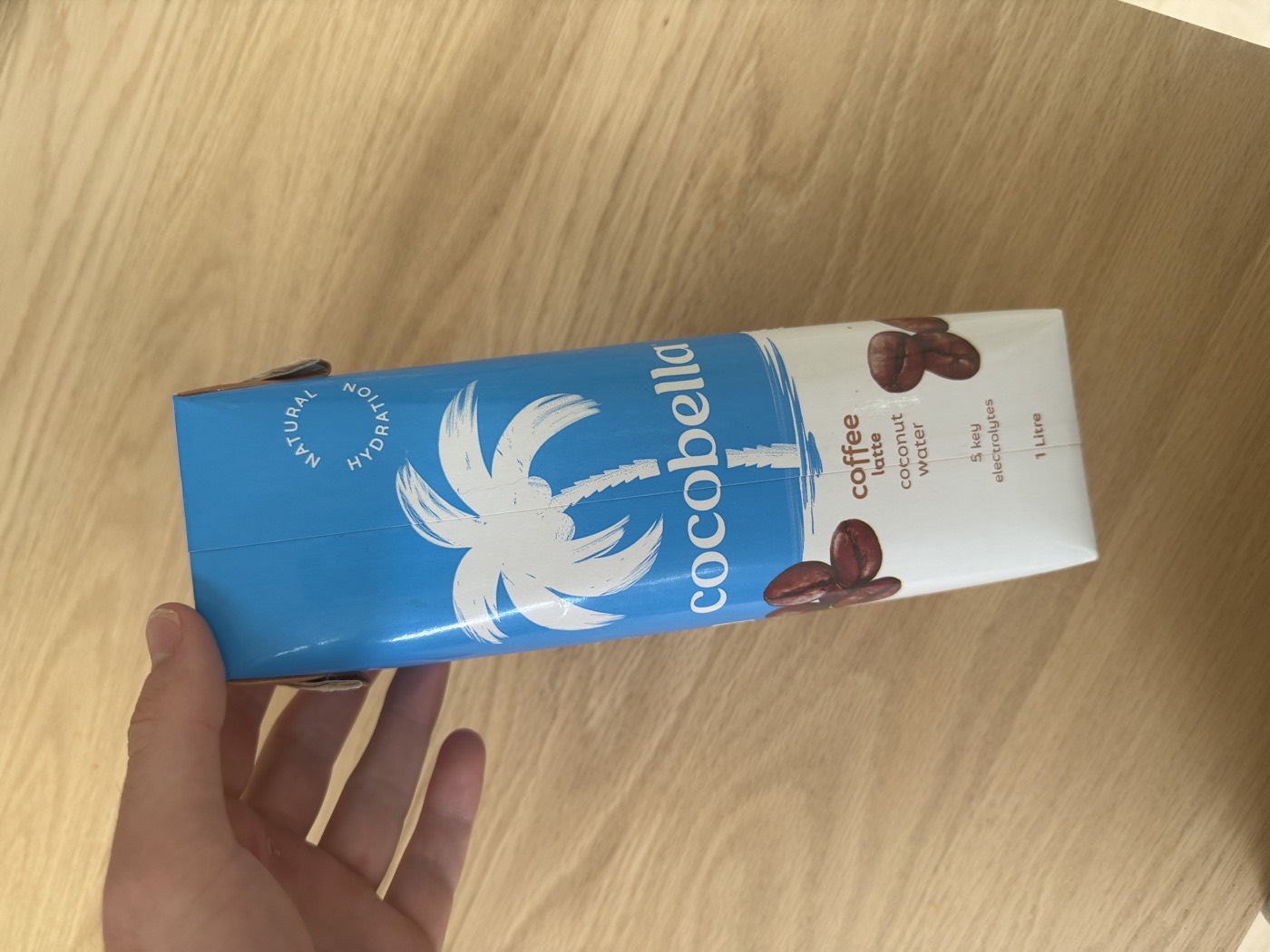 A carton of Cocobella coffee latte coconut water on a wooden table.